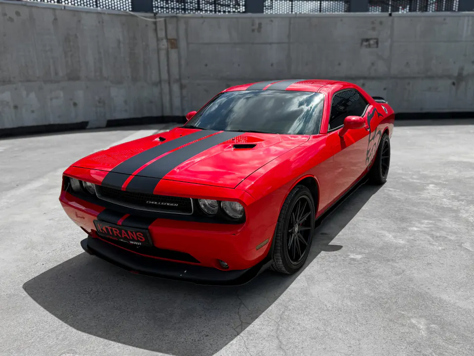 Red 2013 Dodge Challenger with black stripes and a KTRANS plate on a concrete parking garage roof