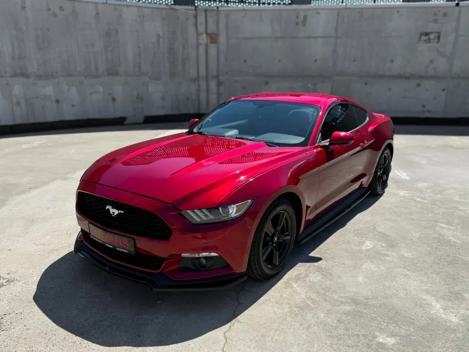 Red 2015 Ford Mustang with a KTRANS plate on a concrete parking garage roof