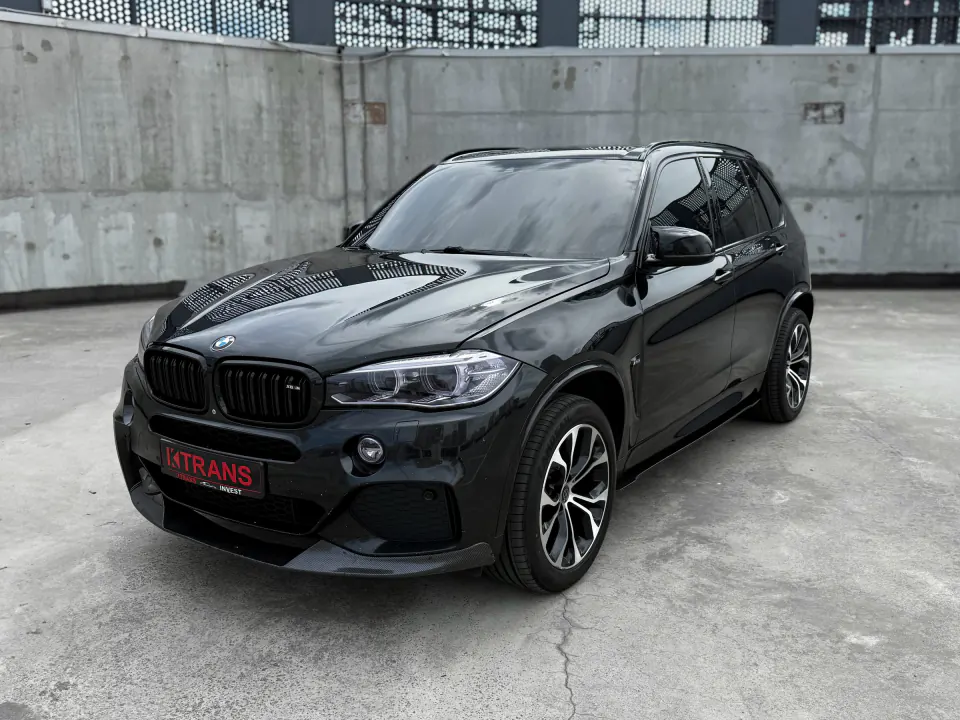 Black 2014 BMW X5 with a KTRANS plate on a concrete parking garage roof