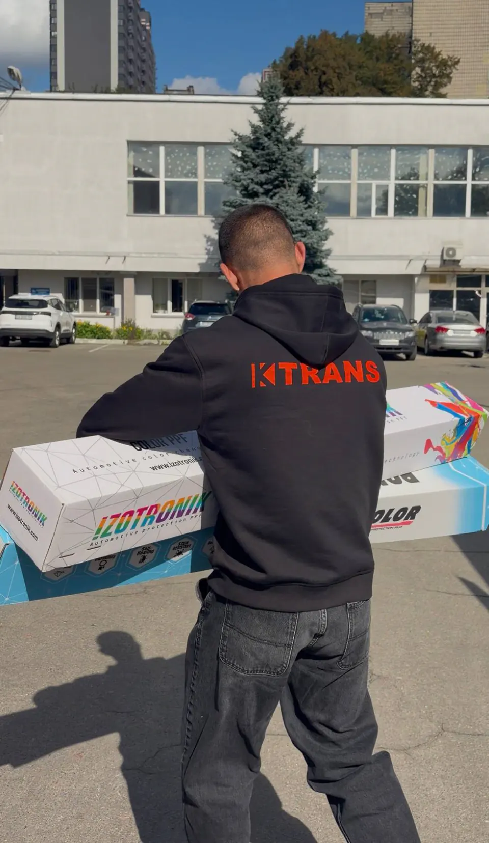 Employee in a black KTRANS hoodie carrying boxes, seen from behind