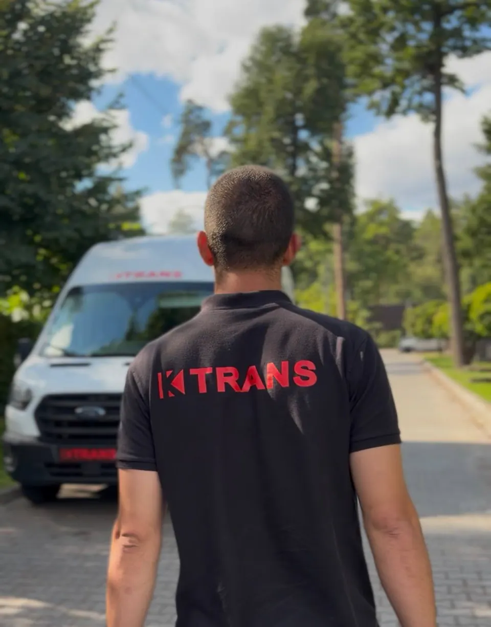 Employee in a black KTRANS polo shirt, seen from behind, next to a white KTRANS Ford Transit